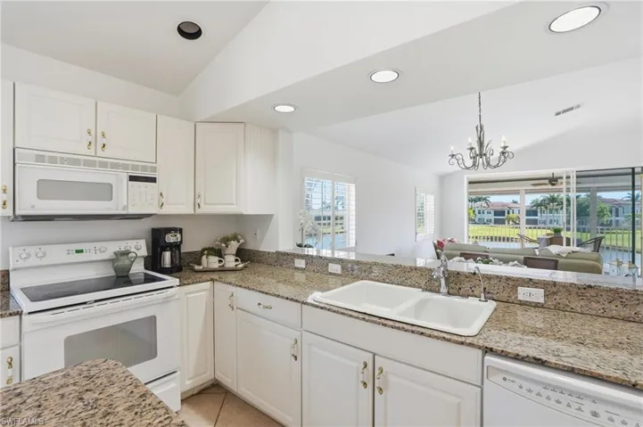 Kitchen featuring white cabinetry, granite countertops, a double basin sink, and white appliances