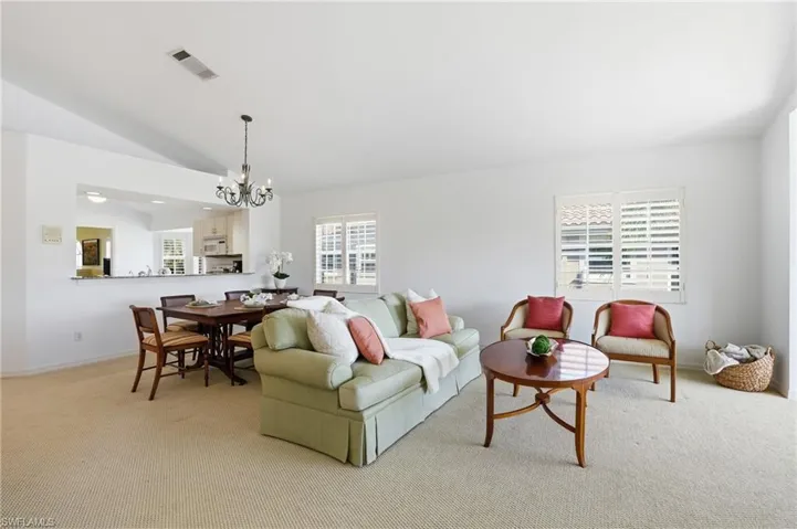 Open-concept living area with neutral carpeting, white walls, and vaulted ceilings