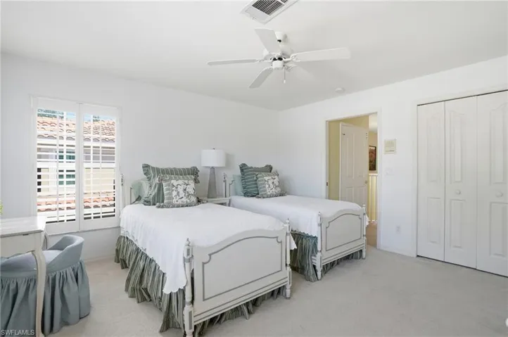 Light-filled bedroom featuring a window with plantation shutters, ceiling fan, carpet flooring, and bi-fold closet doors