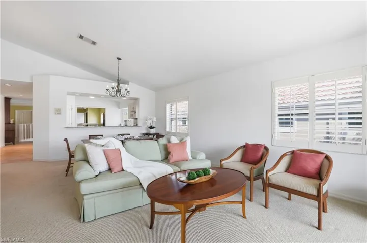 Vaulted ceilings enhance this open living space featuring light-colored carpeting, white walls, and window shutters