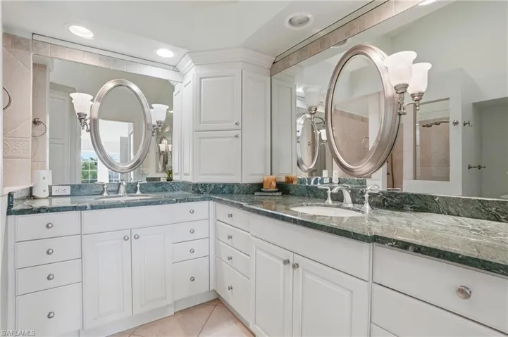 Dual vanity featuring white cabinetry, green stone countertops, oval mirrors, and recessed lighting