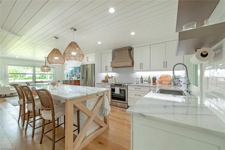 Kitchen with pendant lighting, custom exhaust hood, sink, appliances with stainless steel finishes, and white cabinetry