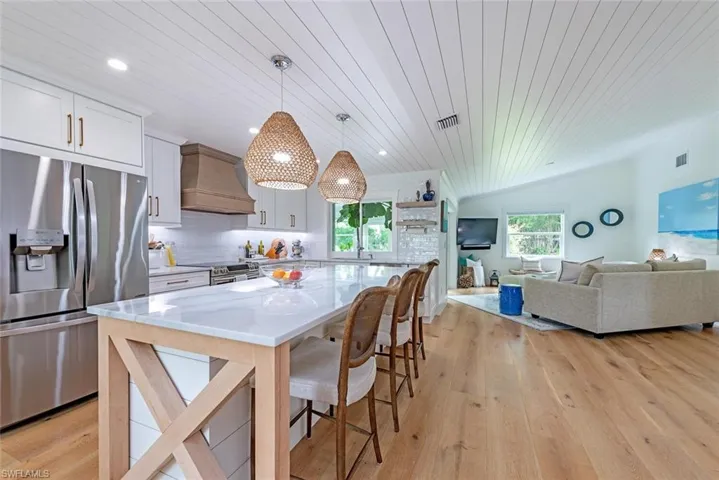 Kitchen featuring white cabinetry, hanging light fixtures, a kitchen island, custom range hood, and appliances with stainless steel finishes