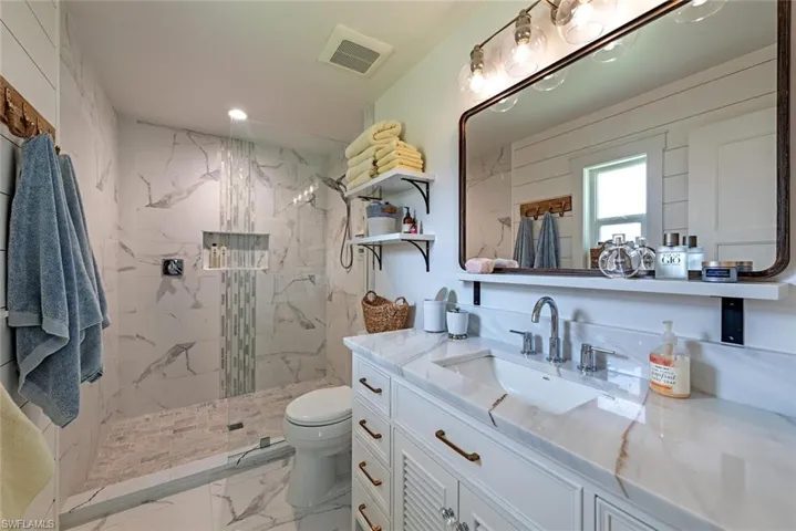 Bathroom with toilet, a tile shower, and vanity