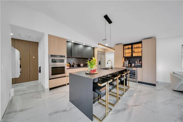 Kitchen with two tone cabinets, a breakfast bar, decorative light fixtures, a kitchen island with sink, and wine cooler