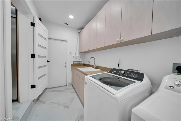 Laundry room with cabinet space, light marble finish flooring, washing machine and clothes dryer, and recessed lighting