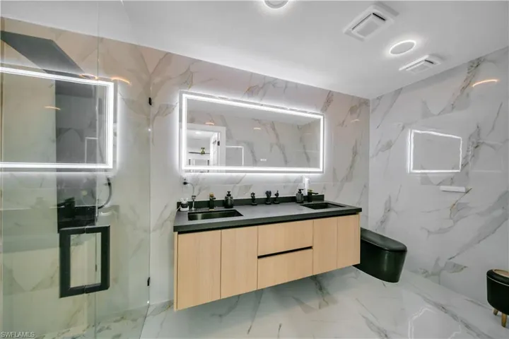 Bathroom featuring a marble finish shower, stone wall, double vanity, tile walls, and light marble finish flooring