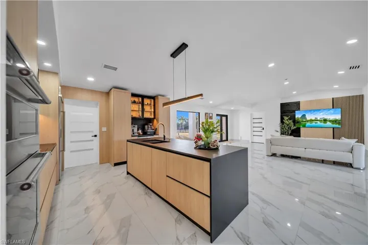Kitchen with light wood finish cabinets, glass insert cabinets, a kitchen island with sink, open floor plan, and double oven