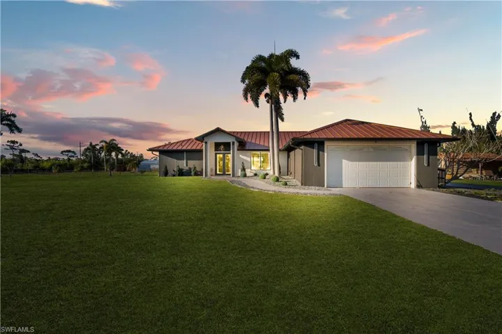 View of front of home with a front yard, driveway, a metal roof, and a garage