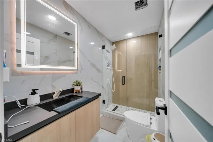 Bathroom with a marble finish shower, vanity, recessed lighting, and tile walls