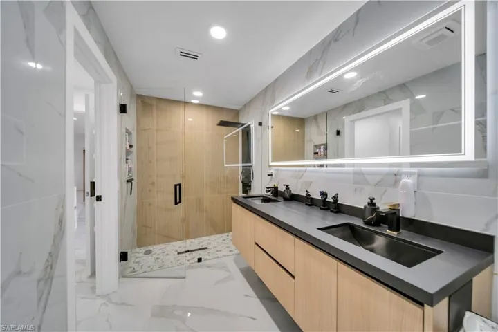 Full bath with double vanity, a shower stall, tile walls, light marble finish flooring, and recessed lighting