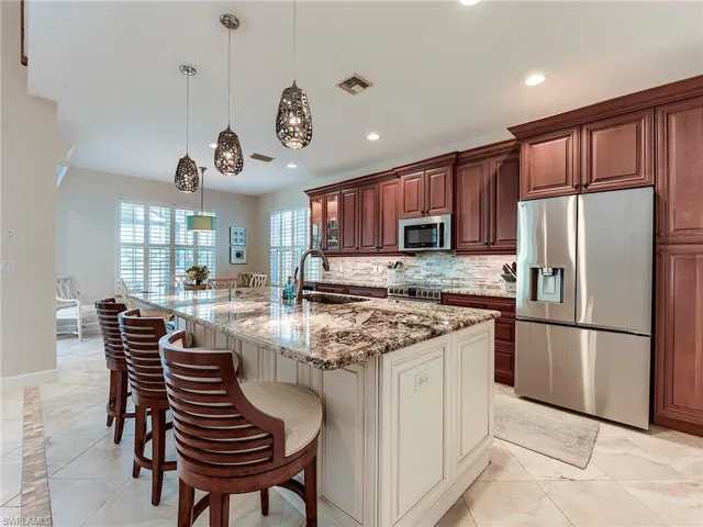 Kitchen featuring stainless steel appliances, a kitchen bar, pendant lighting, light stone counters, and a kitchen island with sink
