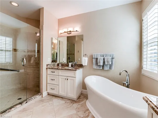 Bathroom featuring vanity, a freestanding bath, a stall shower, and light marble finish floors