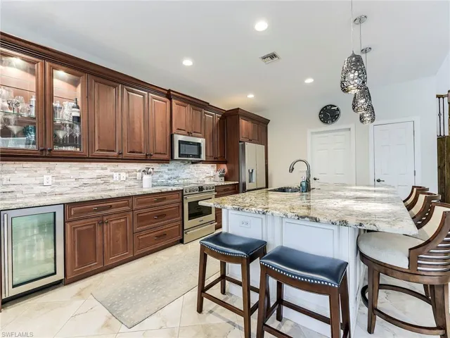 Kitchen with a kitchen breakfast bar, beverage cooler, decorative light fixtures, light stone countertops, and appliances with stainless steel finishes