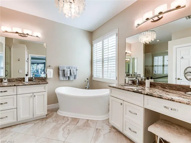 Bathroom with a chandelier, a stall shower, two vanities, a freestanding bath, and a textured wall