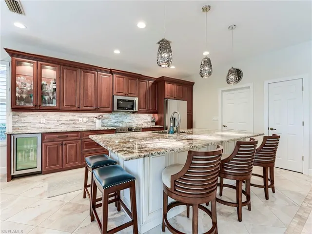 Kitchen with a breakfast bar area, hanging light fixtures, light stone countertops, wine cooler, and appliances with stainless steel finishes