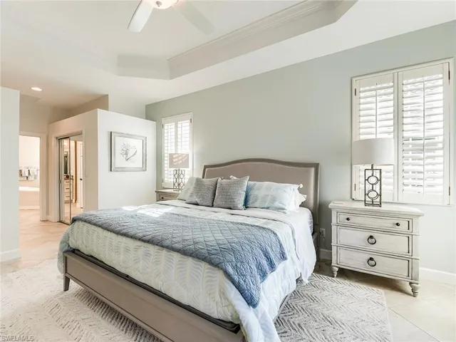 Bedroom featuring light tile patterned floors, a tray ceiling, ornamental molding, ceiling fan, and ensuite bath