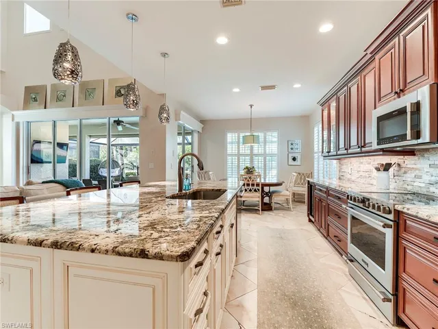 Kitchen featuring hanging light fixtures, stainless steel appliances, light stone counters, a large island with sink, and recessed lighting