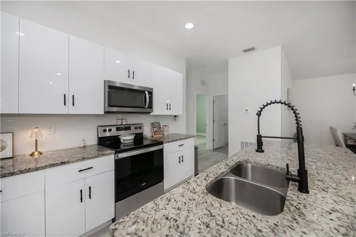 Kitchen with stainless steel appliances, white cabinetry, light stone countertops, decorative backsplash, and light wood finished floors