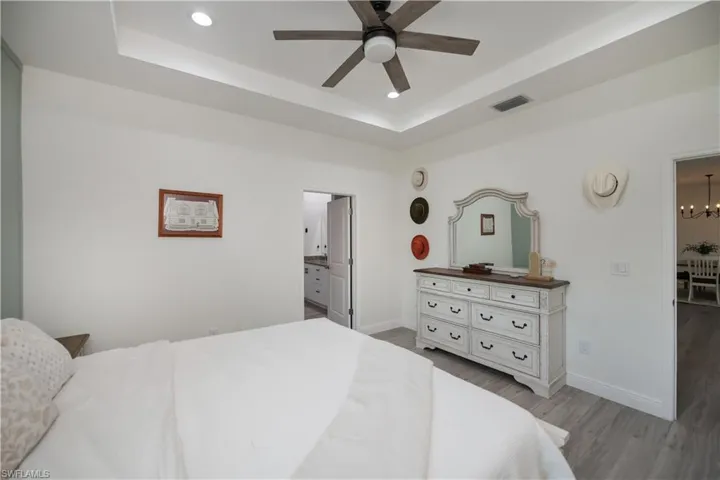 Bedroom with a raised ceiling, light wood-style flooring, a ceiling fan, ensuite bathroom, and hanging lights