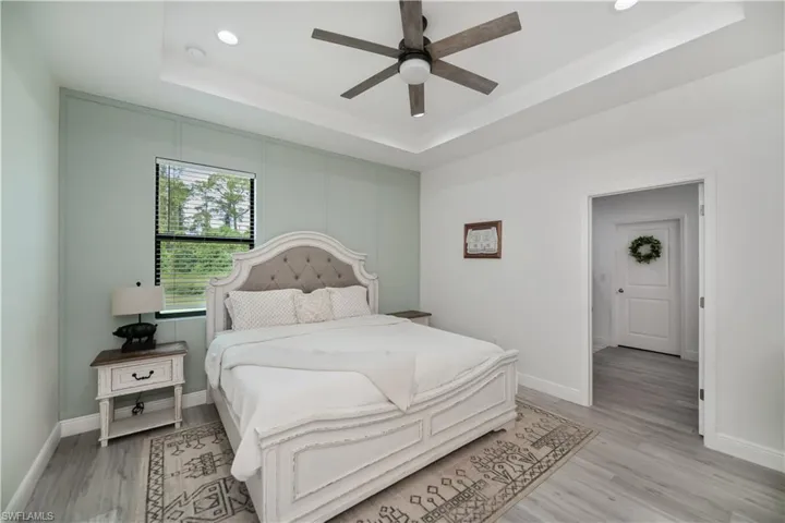 Bedroom featuring a raised ceiling, a ceiling fan, light wood finished floors, and recessed lighting
