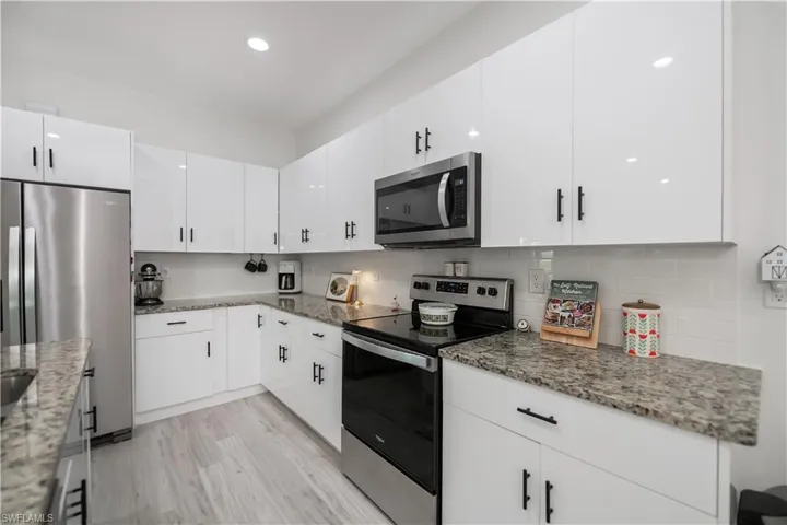 Kitchen featuring stainless steel appliances, white cabinets, light stone counters, light wood-type flooring, and recessed lighting