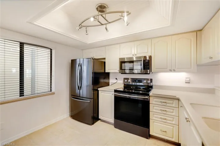 Kitchen featuring stainless steel appliances, a raised ceiling, light countertops, and light tile patterned flooring