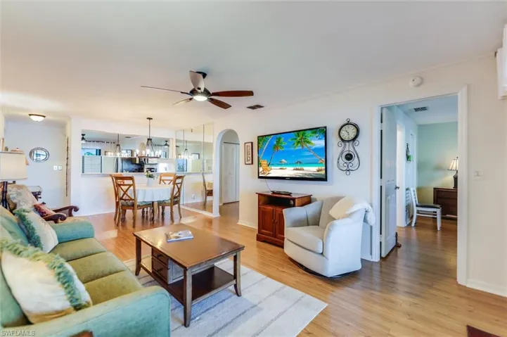 Living room with arched walkways, wood finished floors, ceiling fan, and a chandelier