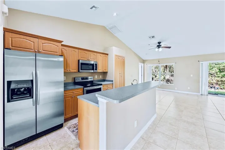 Kitchen featuring lofted ceiling, ceiling fan, light tile patterned floors, an island with sink, and stainless steel appliances