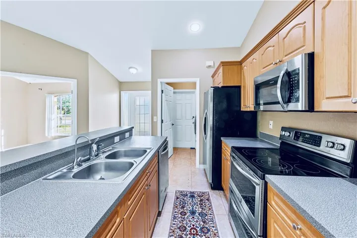 Kitchen featuring sink, light tile patterned floors, stainless steel appliances, and vaulted ceiling