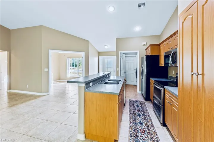 Kitchen featuring stainless steel appliances, vaulted ceiling, a kitchen island with sink, and sink