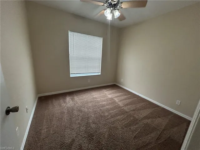 Empty room featuring ceiling fan and dark carpet