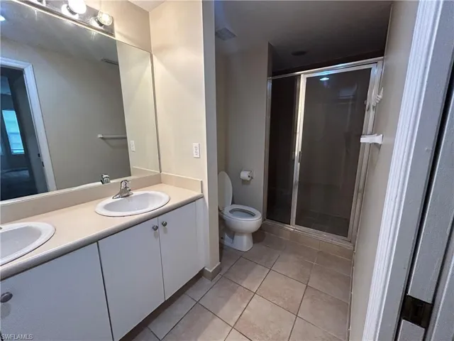 Full bath featuring double vanity, a shower stall, and light tile patterned floors
