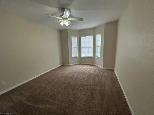 Empty room with a textured wall, a ceiling fan, and dark carpet
