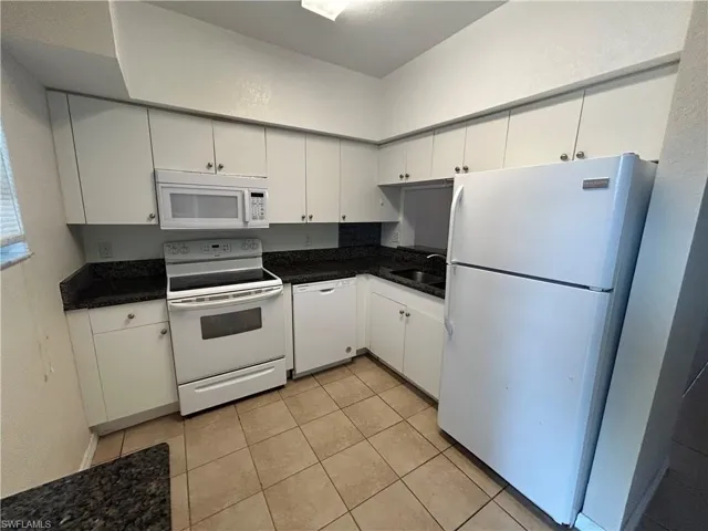Kitchen featuring white appliances, white cabinets, light tile patterned floors, and a textured wall