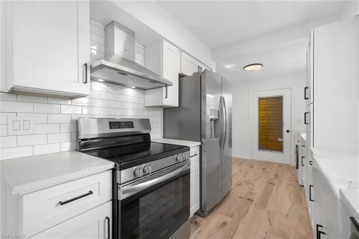 Kitchen with light wood-style flooring, wall chimney range hood, white cabinetry, appliances with stainless steel finishes, and decorative backsplash
