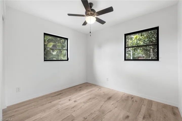 Empty room with wood finished floors, baseboards, a ceiling fan, and plenty of natural light
