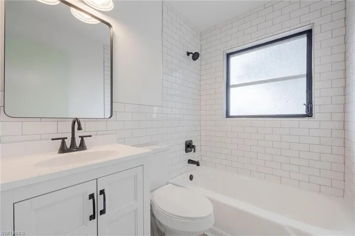 Full bathroom featuring vanity, toilet, tile walls, decorative backsplash, and shower / bathing tub combination