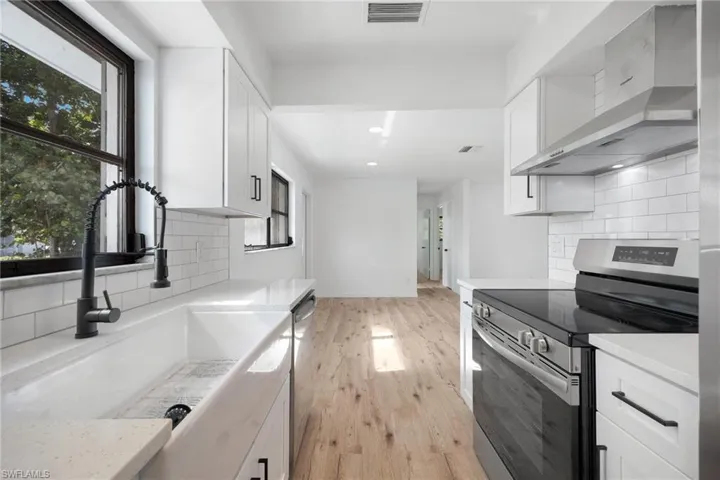 Kitchen with wall chimney range hood, white cabinets, a sink, and appliances with stainless steel finishes