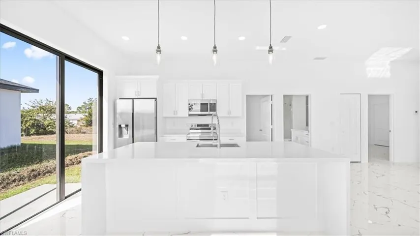 Kitchen with white cabinetry, stainless steel appliances, pendant lighting, and light stone counters
