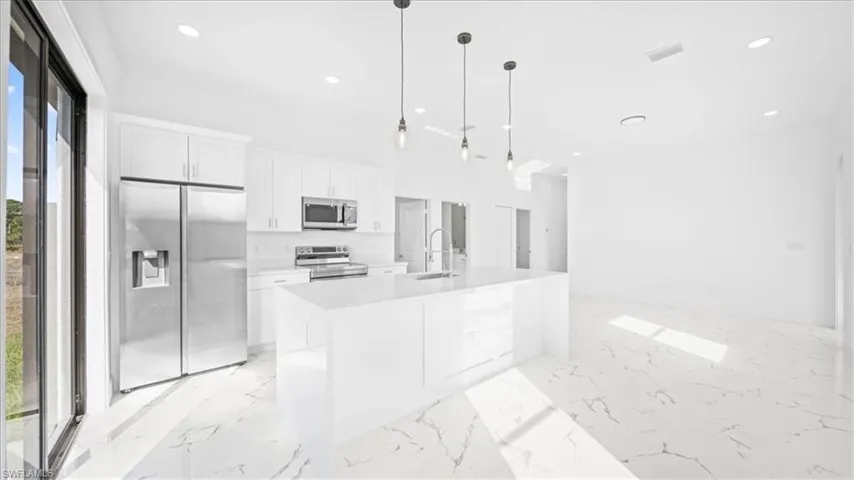 Kitchen featuring stainless steel appliances, white cabinets, decorative light fixtures, a kitchen island with sink, and light stone countertops