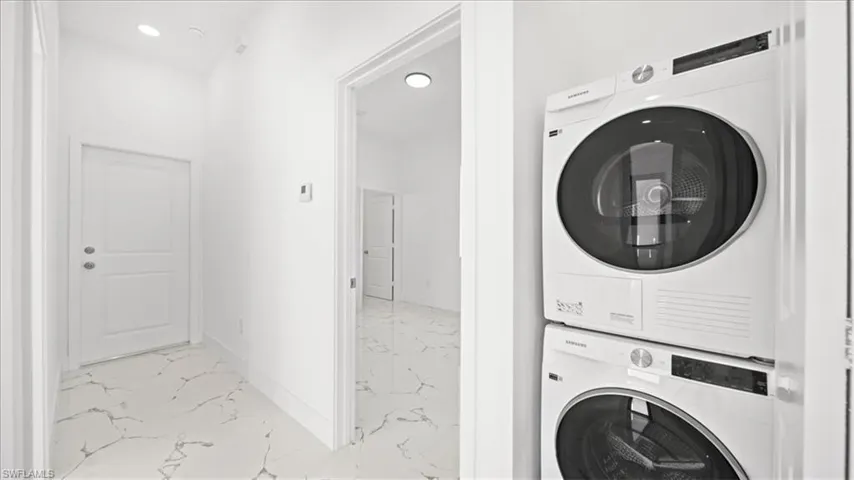 Laundry area with stacked washer / drying machine, light marble finish flooring, and recessed lighting