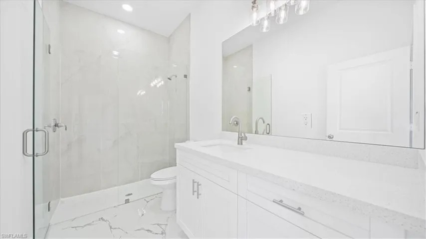Bathroom with vanity, a marble finish shower, and recessed lighting