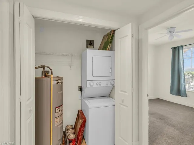 Washroom featuring electric water heater, ceiling fan, carpet flooring, and stacked washer / drying machine