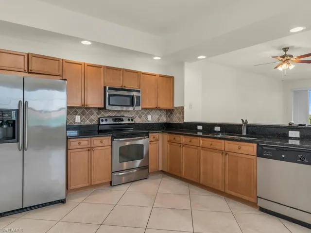 Kitchen featuring ceiling fan, sink, appliances with stainless steel finishes, light tile patterned floors, and backsplash