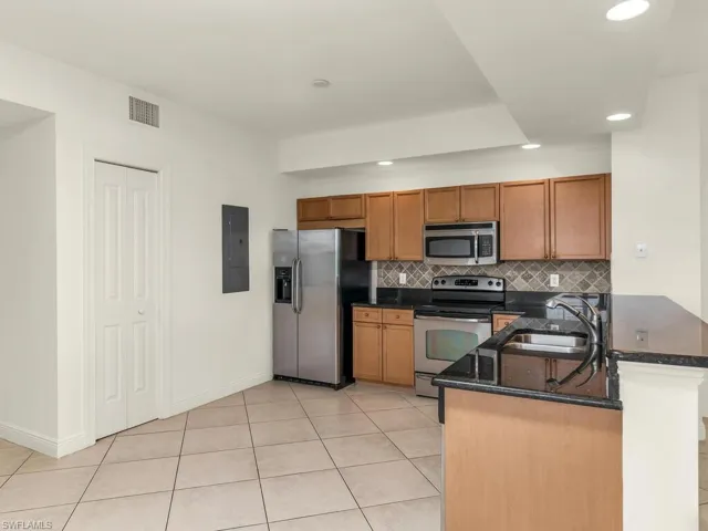 Kitchen featuring light tile patterned floors, kitchen peninsula, appliances with stainless steel finishes, decorative backsplash, and sink