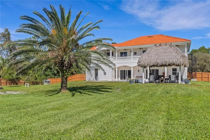 Rear view of property with a patio, a balcony, a tiled roof, fence, and a yard
