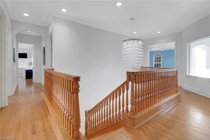 Corridor featuring light wood-style floors, recessed lighting, arched walkways, and an upstairs landing