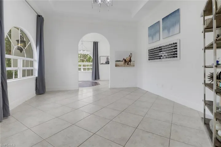 Empty room featuring a tray ceiling, arched walkways, baseboards, and light tile patterned floors