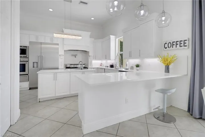 Kitchen featuring light countertops, hanging light fixtures, white cabinets, built in appliances, and a peninsula